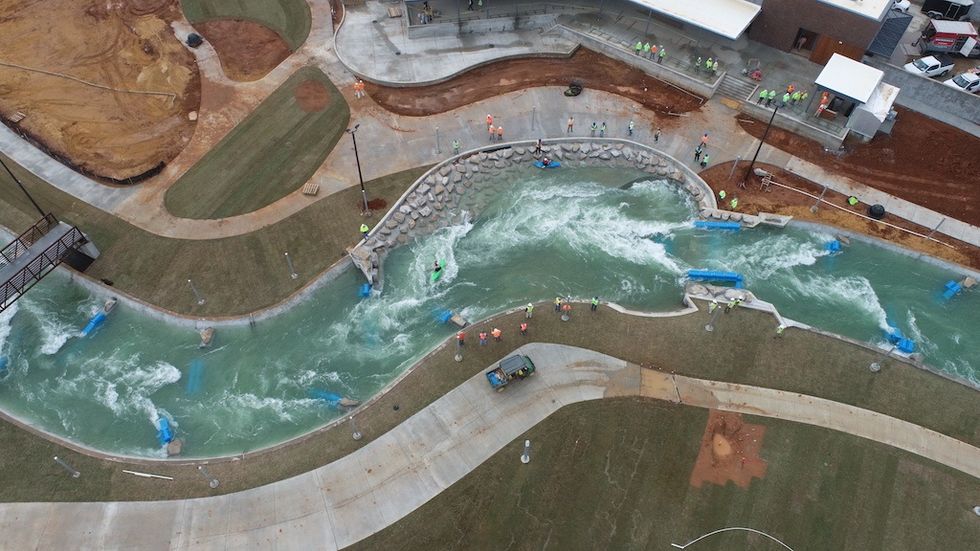 Aerial view of a winding artificial whitewater rafting course in a green landscape.
