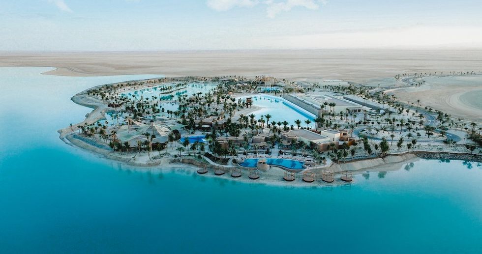 Aerial view of Adrena resort with pools surrounded by water and palm trees.