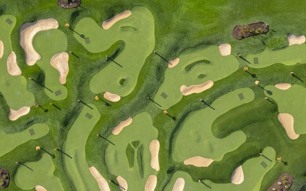 Aerial view of an abstractly designed golf course with diverse green shapes and sand traps.