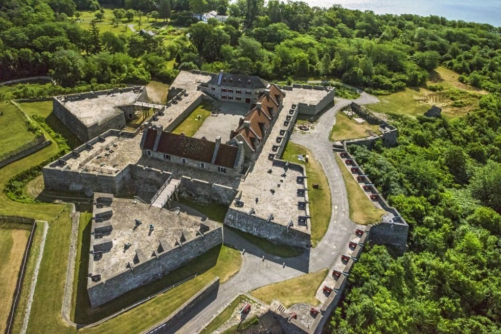 Aerial view of an old stone fort surrounded by lush green trees and grass.
