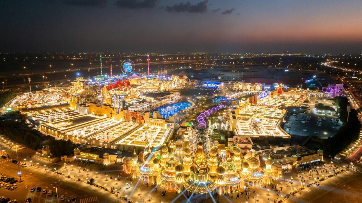 Aerial view of brightly lit theme park called Global Village at dusk, with colorful lights and Ferris wheel.