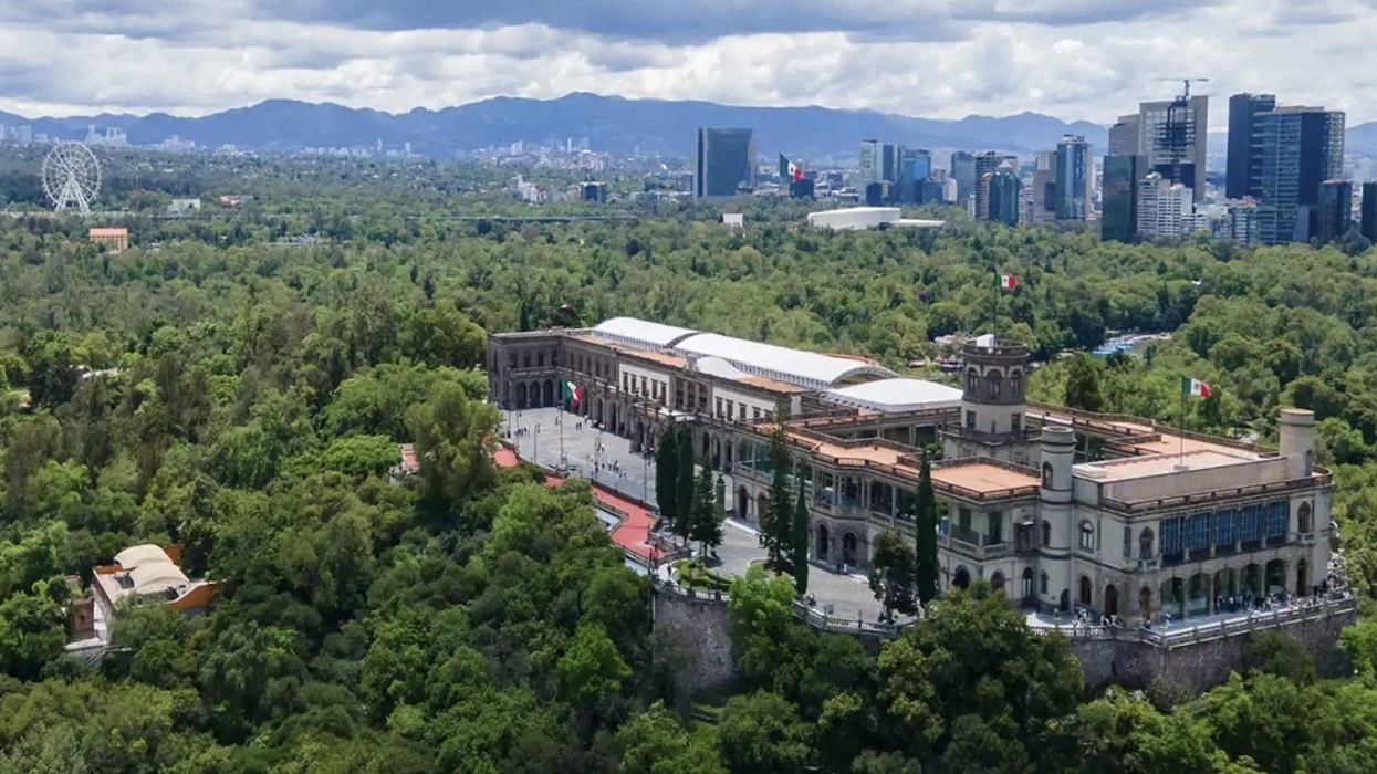 Aerial view of Chapultepec Castle amid lush greenery with city skyline in the background.