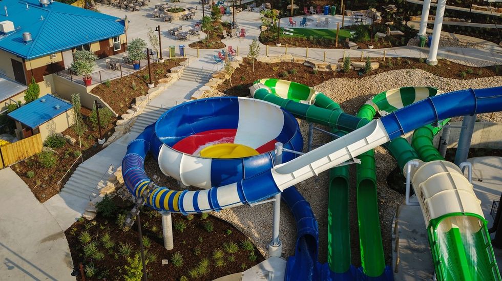 Aerial view of colorful water slides in an outdoor water park with nearby pathways.