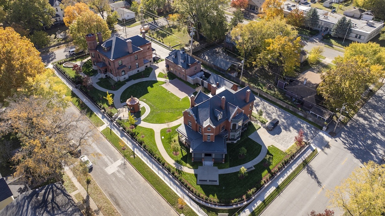 Aerial view of large red-brick historic mansion and gardens, surrounded by autumn trees.