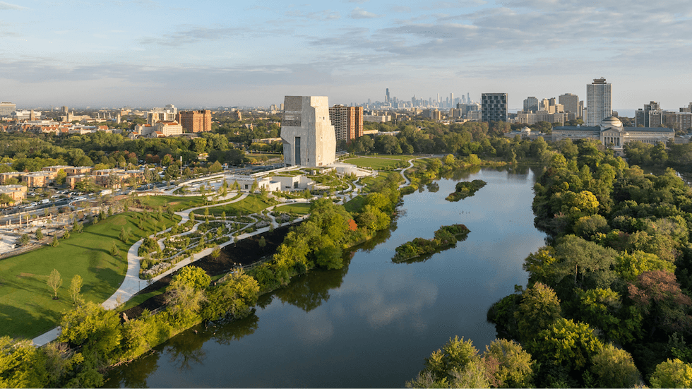 Aerial view of Obama Presidential Center with park, river, and Chicago city skyline under a cloudy sky.