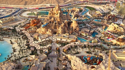 Aerial view of sprawling desert water park with pools, slides, and a mountain-like structure.