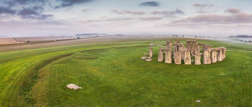 Aerial view of Stonehenge on a foggy morning, surrounded by green fields.