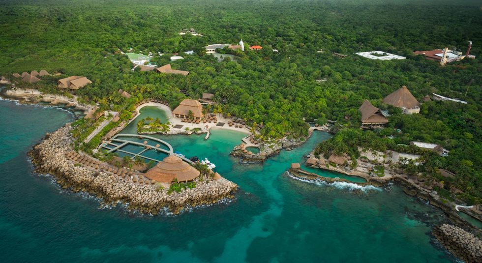 Aerial view of tropical island resort called Parque Xcaret with lush greenery and turquoise waters.