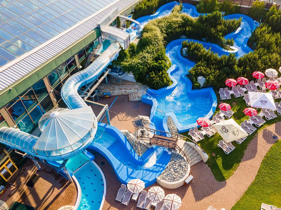 Aerial view of \u200bAquapalace Prague waterpark with slides, lazy river, and sunbathing area with umbrellas and chairs.