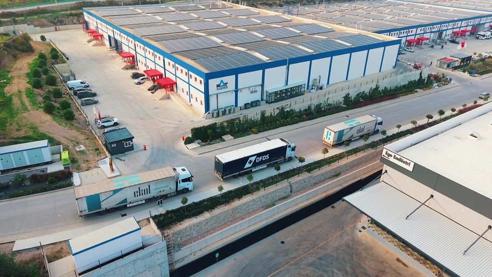 Aerial view of warehouse with solar panels and parked trucks in an industrial area.
