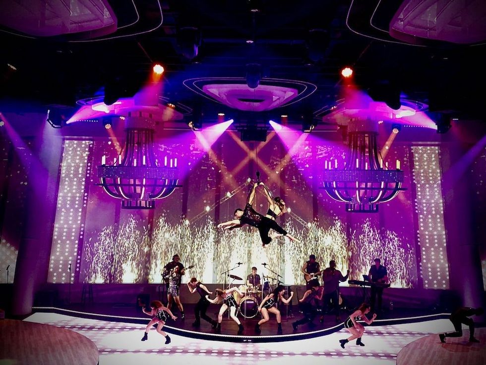Aerialists and musicians perform on a vibrant stage with dramatic lighting.