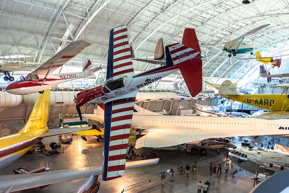 Aircraft displayed in a spacious museum, including a Concorde and aerobatic planes.