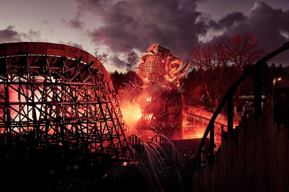 Alton Towers Wickerman wooden roller coaster at sunset, featuring a large, fiery wicker sculpture.