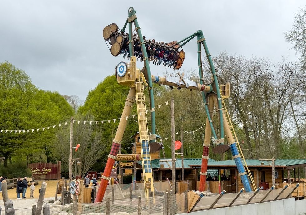 Amusement park ride, Seesaw Swing at Bellewaerde, swings high, with people onboard, surrounded by trees.