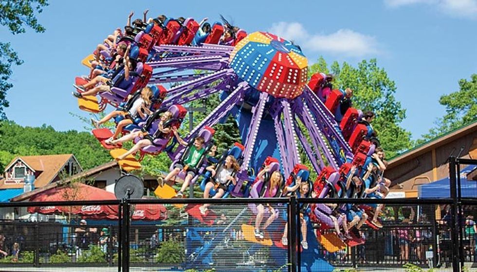 Amusement park ride spinning with people seated, colorful structure, sunny day.