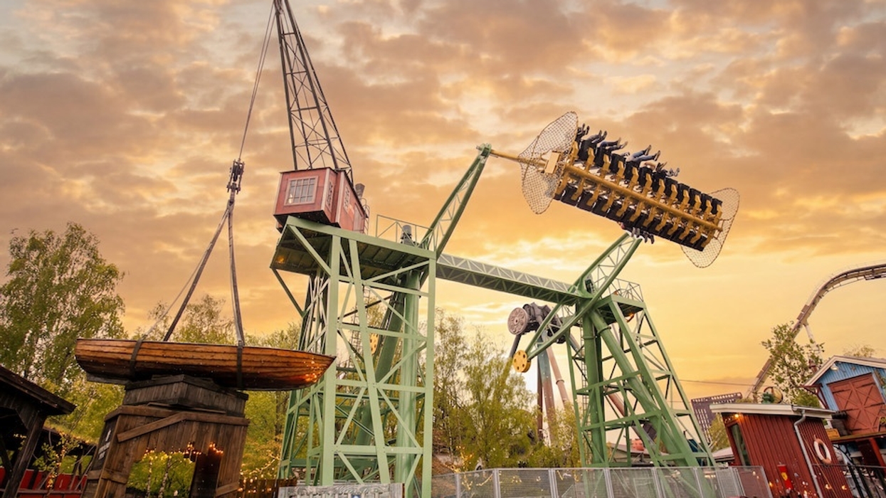 Amusement park ride, Stormvåg at Sweden's Liseberg, shaped like a swinging crane, set against a sunset sky.