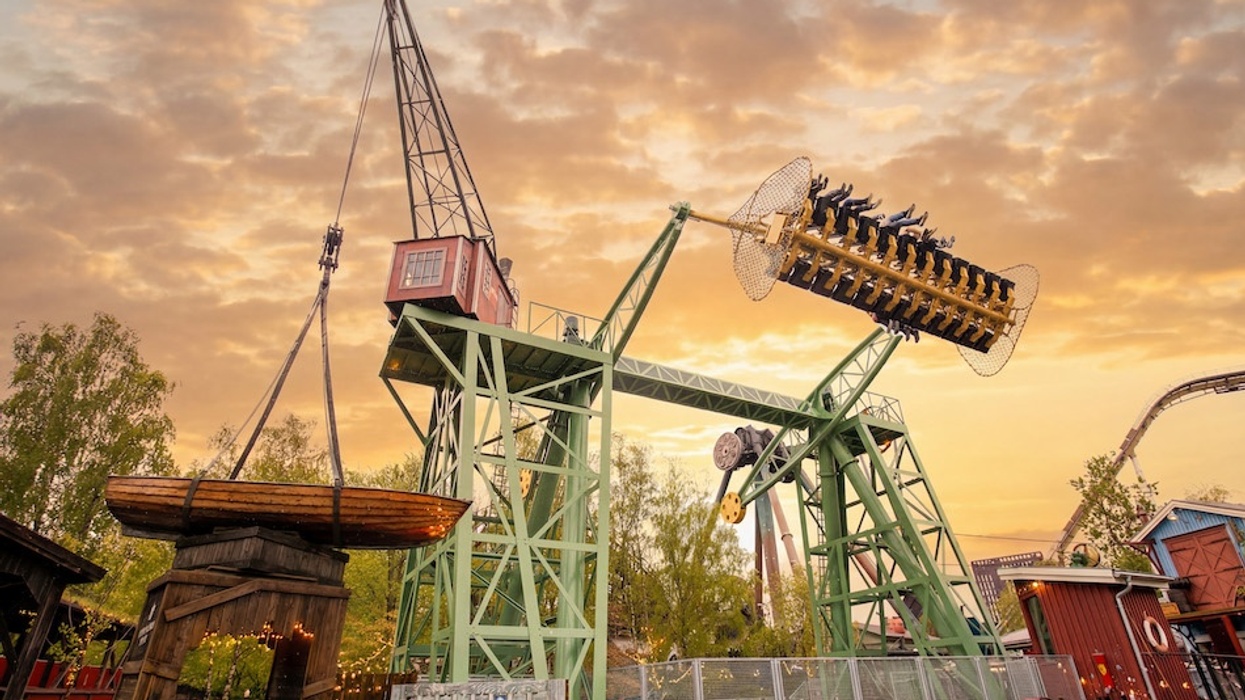 Amusement park ride, Stormvåg at Sweden's Liseberg, shaped like a swinging crane, set against a sunset sky.