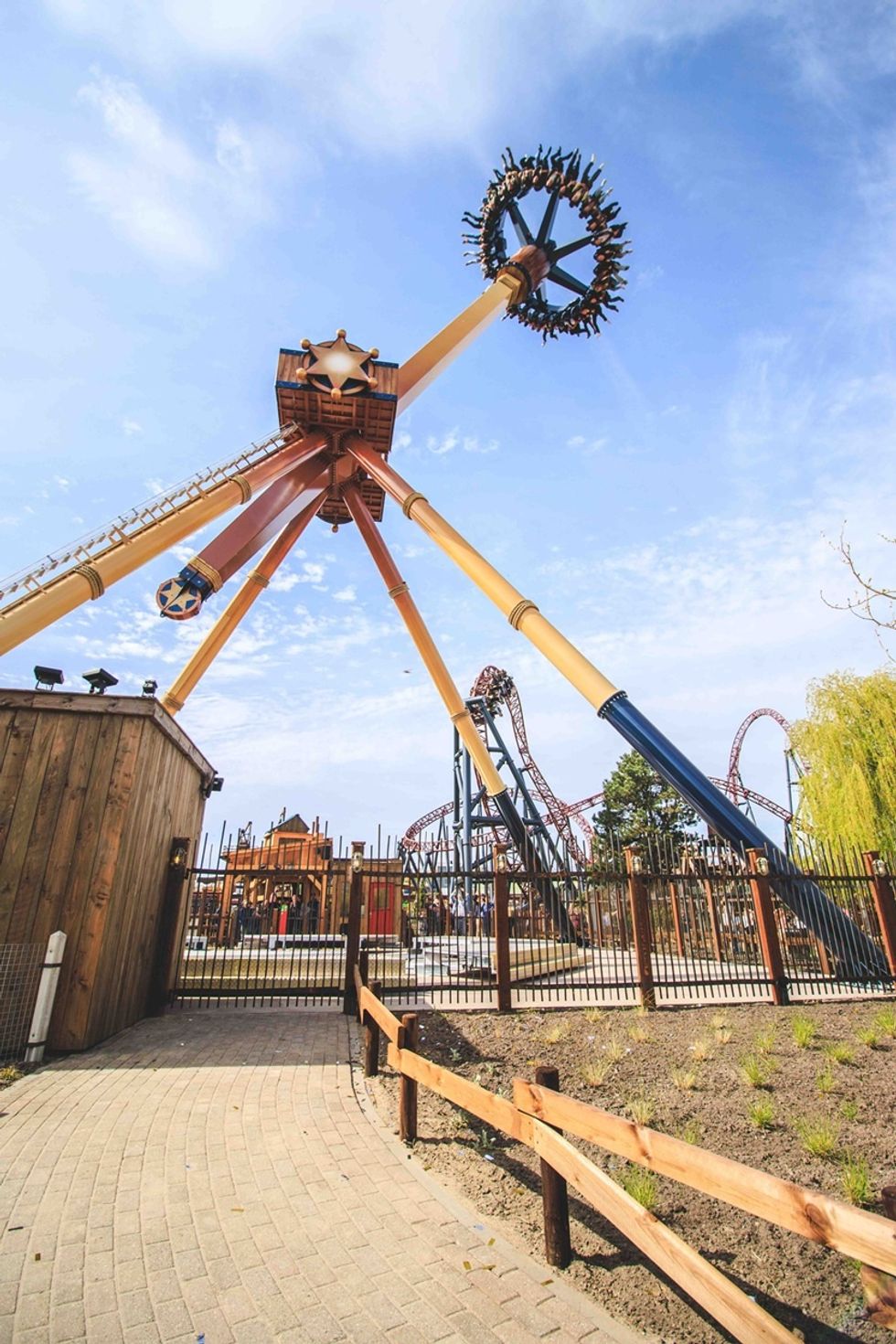 Amusement park ride swings high under a blue sky, with roller coasters in the background.