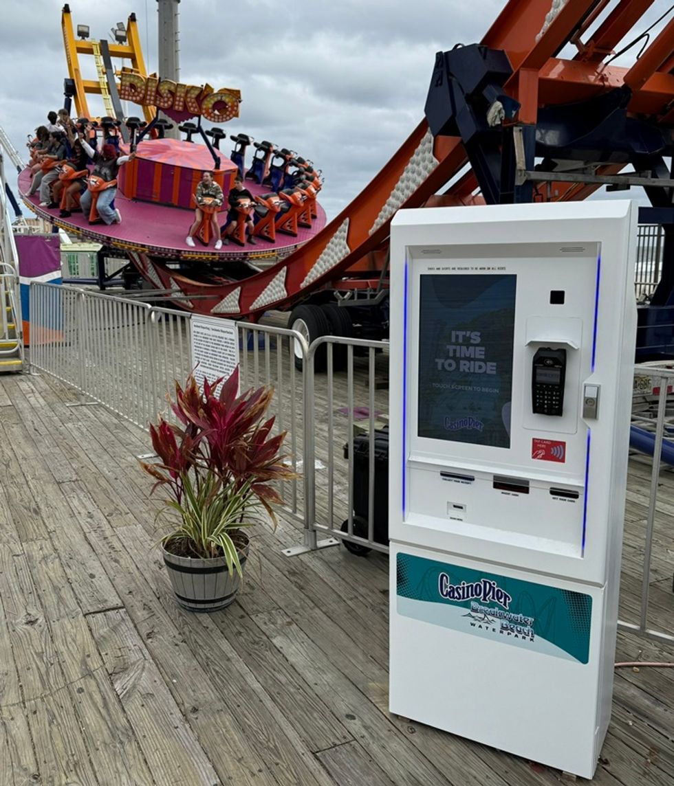 Amusement park ride with kiosk and plant on wooden boardwalk.