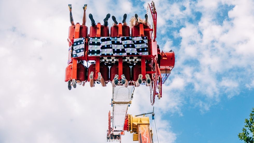 Amusement park ride with people upside down against a cloudy sky background.