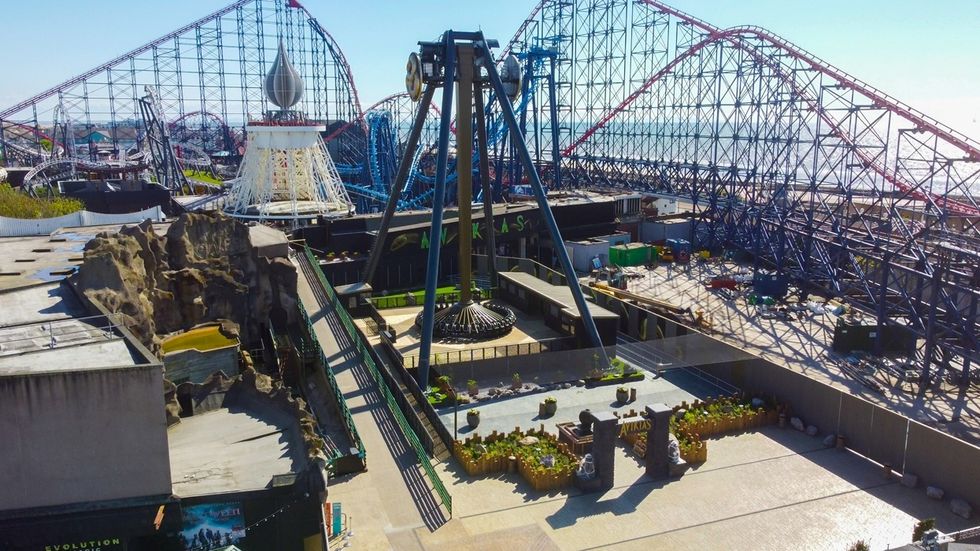 Amusement park with roller coasters and a central swing ride on a sunny day.