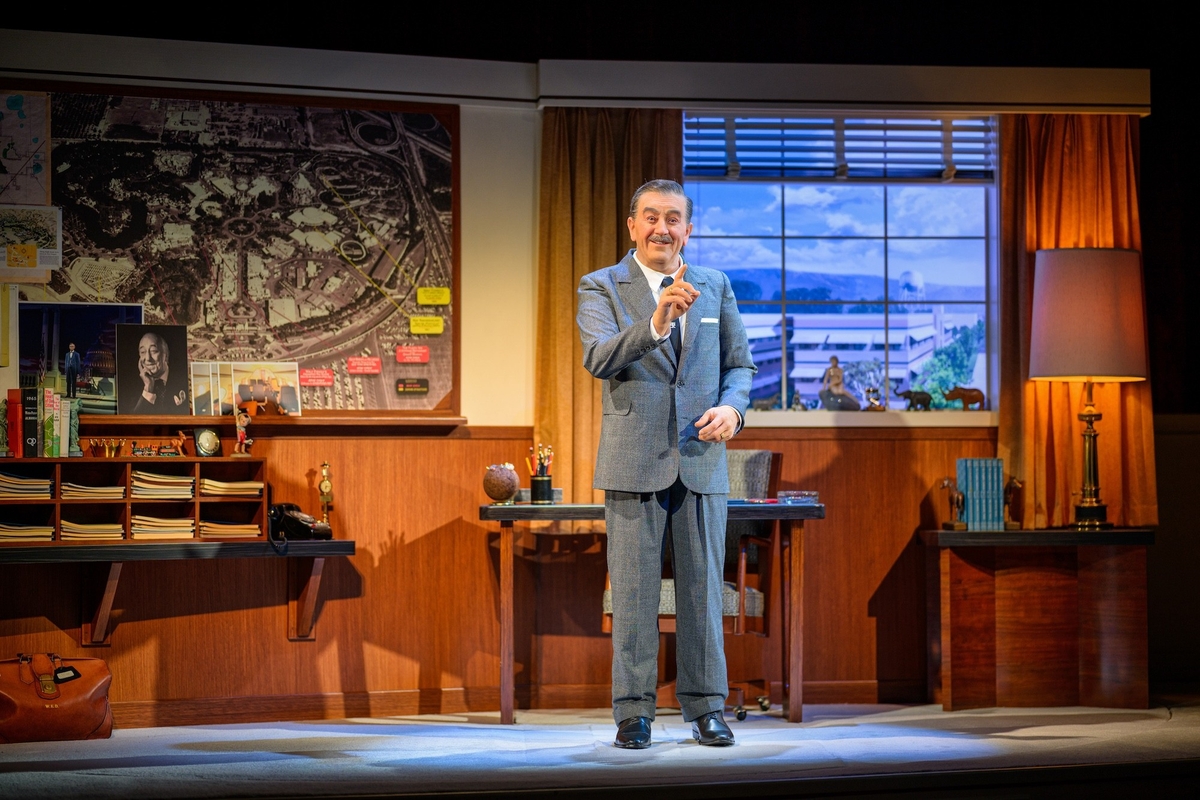 An animatronic of Walt Disney gestures on stage beside a vintage office desk and large map as part of 'Walt Disney - A Magical Life' at Disneyland Resort.