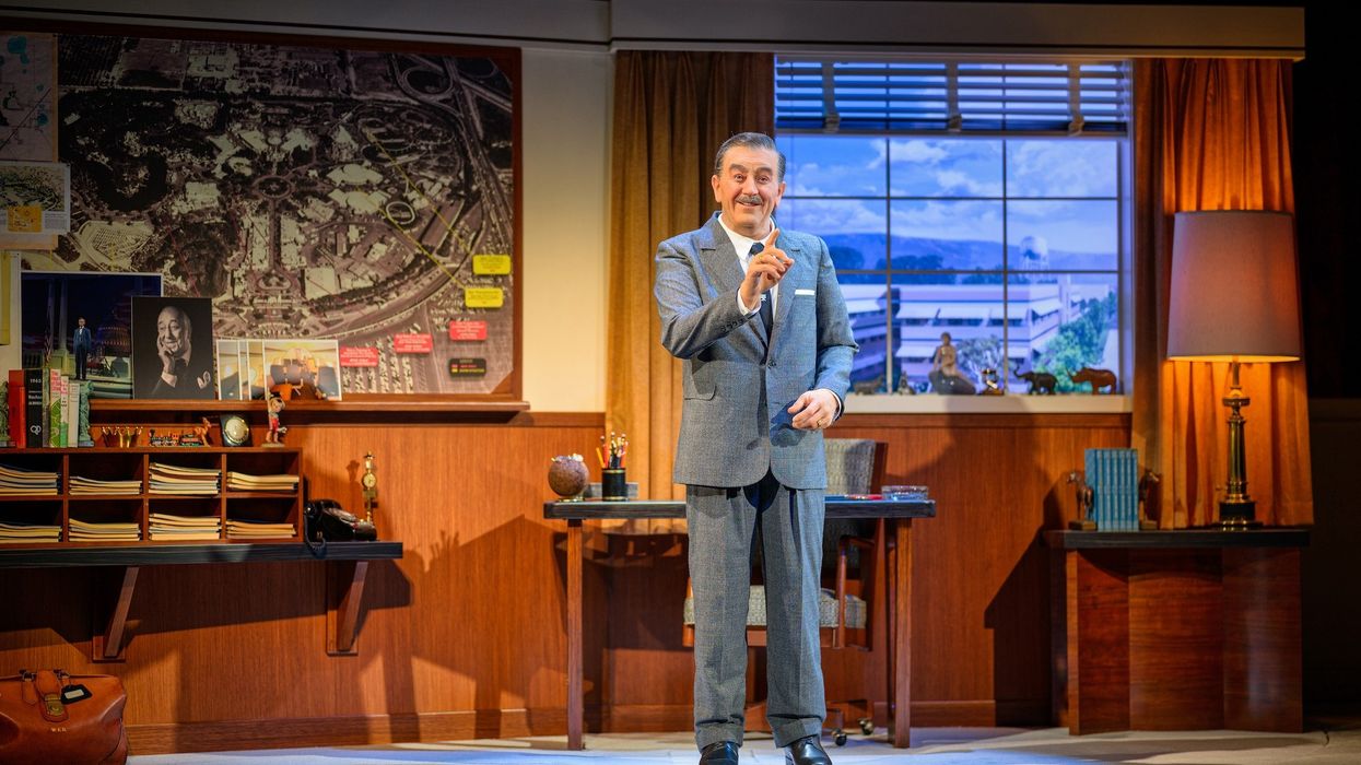 An animatronic of Walt Disney gestures on stage beside a vintage office desk and large map as part of 'Walt Disney - A Magical Life' at Disneyland Resort.