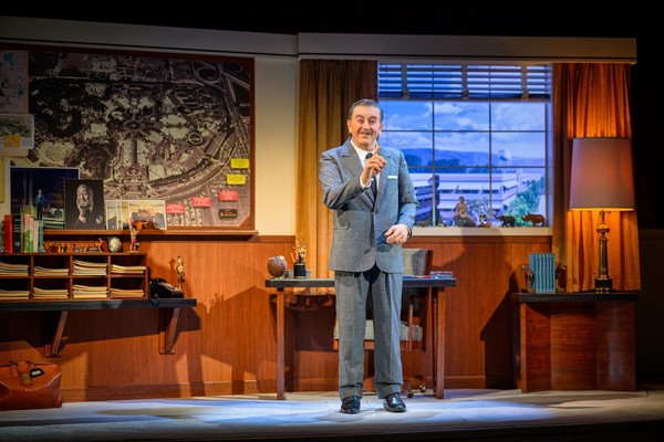 An animatronic of Walt Disney gestures on stage beside a vintage office desk and large map as part of 'Walt Disney - A Magical Life' at Disneyland Resort.