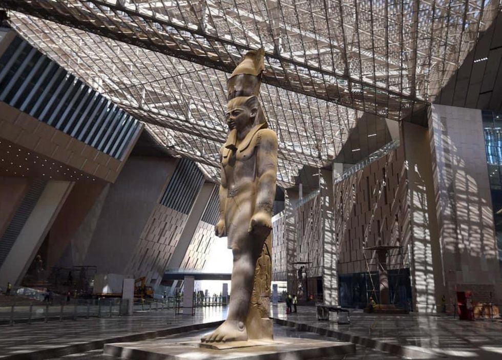 Ancient Egyptian statue in a sunlit modern museum atrium.