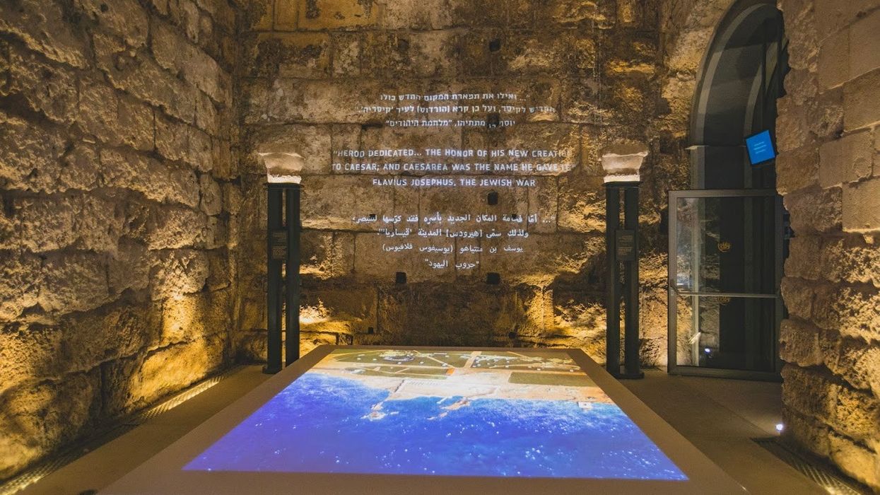 Ancient stone wall with multilingual text and a map display table at Caesarea Harbour Visitor Centre