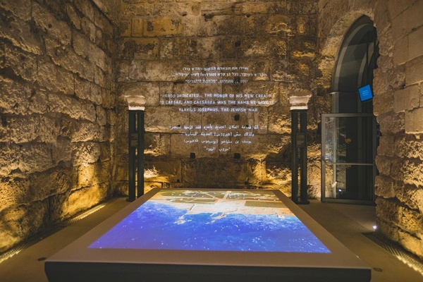 Ancient stone wall with multilingual text and a map display table at Caesarea Harbour Visitor Centre