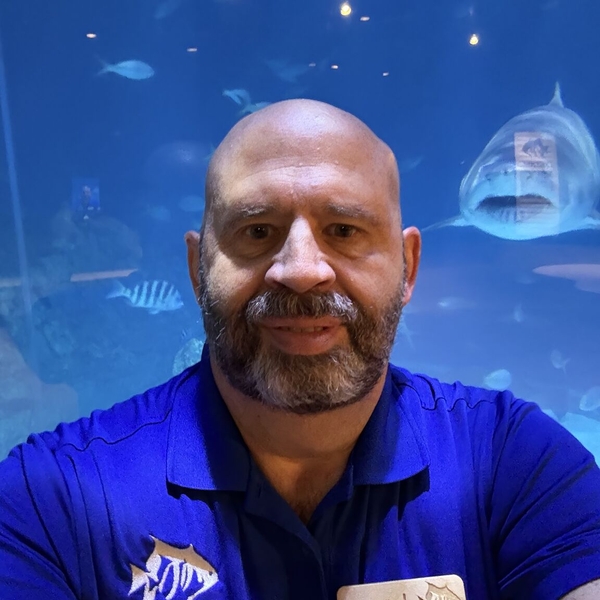 Aquarium staff member in blue shirt with shark in background.