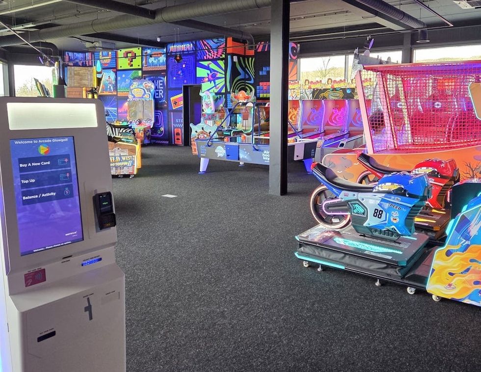 Arcade interior with colorful games, motorcycle ride, and payment kiosk in view.