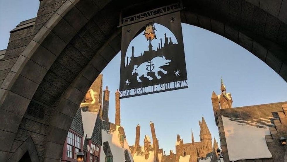 Archway entrance to a theme park village with castle spires in the background.