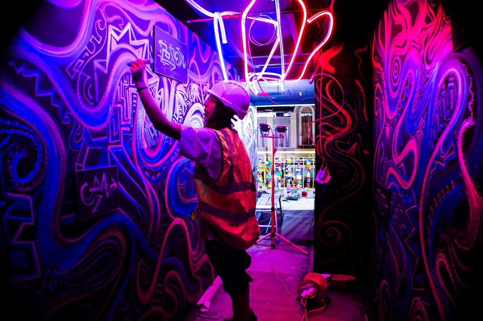 Artist painting vibrant, neon-lit mural in a dimly lit hallway at Absurd City in London