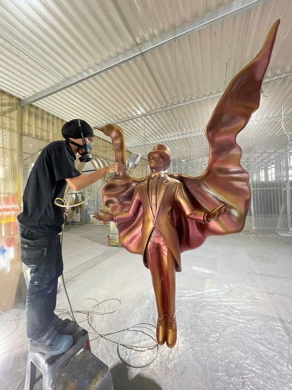 Artist spray-paints metallic sculpture of a winged figure in Pico Play's Vietnam workshop.