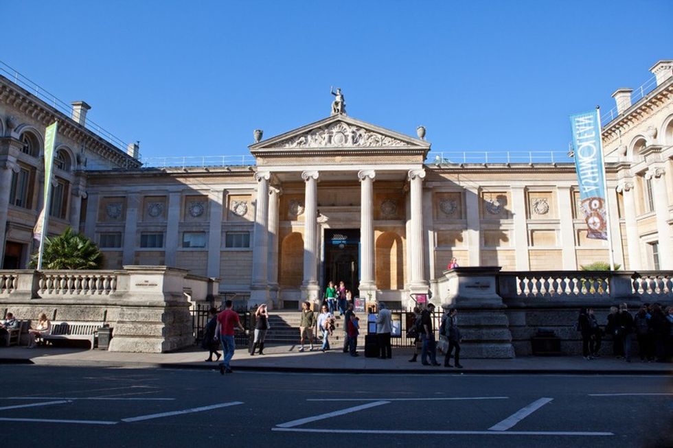 Ashmolean - neoclassical building entrance with columns, people, and banners under a clear blue sky.