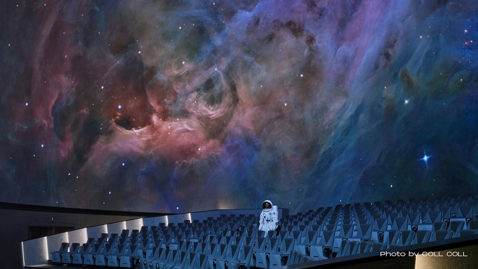 Astronaut in an empty dome theater at Prague Planetarium with a nebula projection immersing them