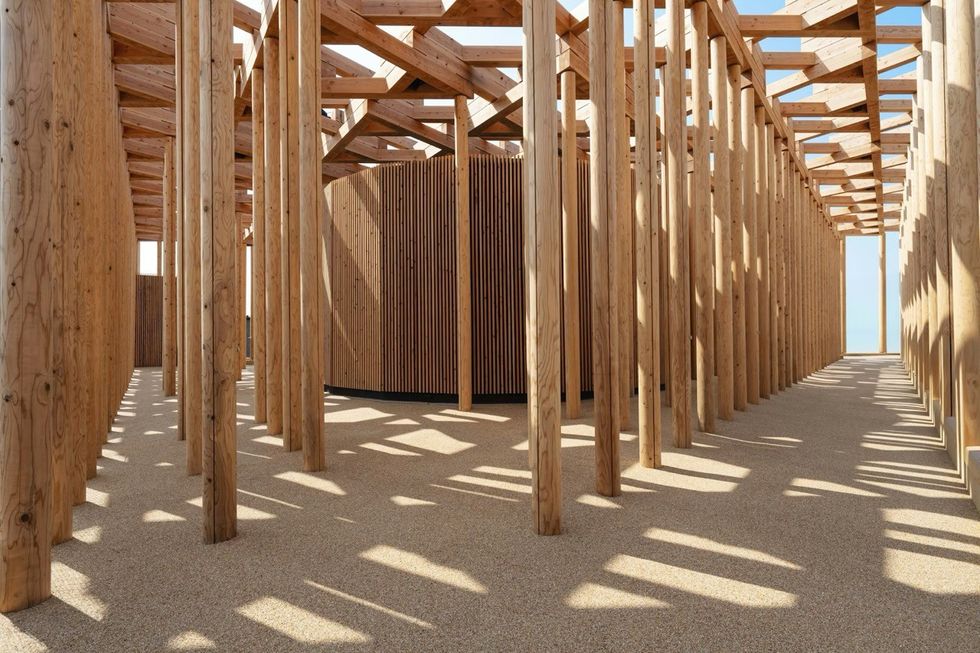 ATELIER BR\u00dcCKNER Uzbekistan Pavilion \u2013 Expo 2025 Osaka Wooden pavilion with vertical beams and geometric shadows, open to a blue sky.