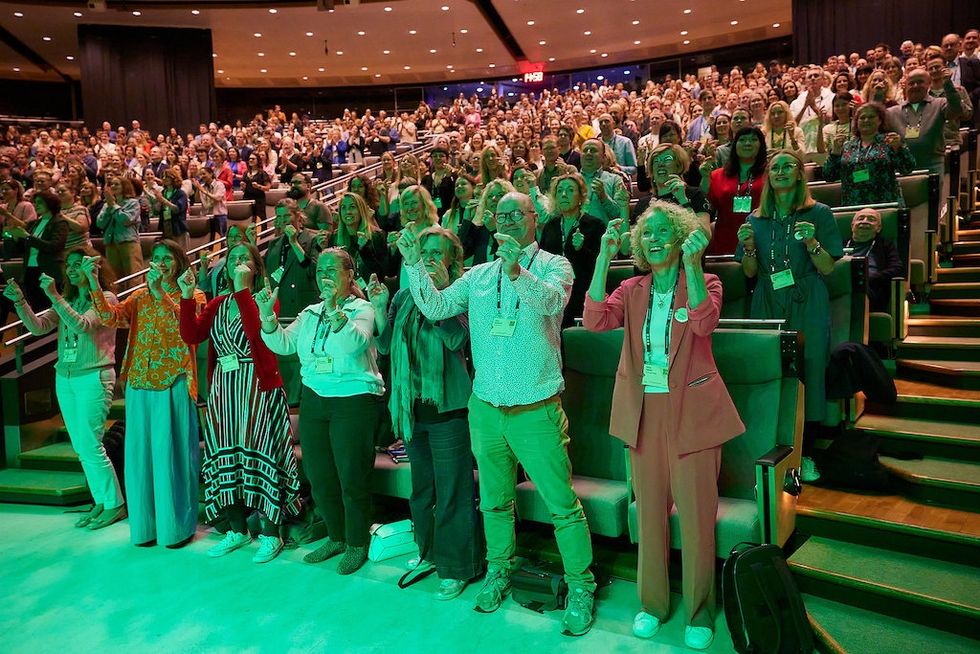 Audience at a conference clapping and smiling, seated and standing in a large auditorium.