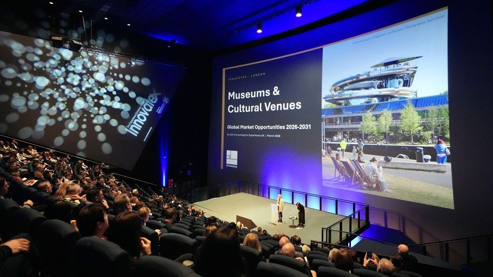 Audience at a conference with a large screen presentation on museums and cultural venues.
