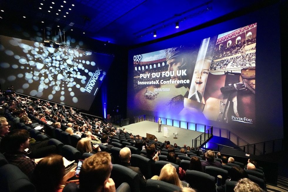 Audience at Puy du Fou session during UK InnovateX Conference in a large theater with a presentation on screen.