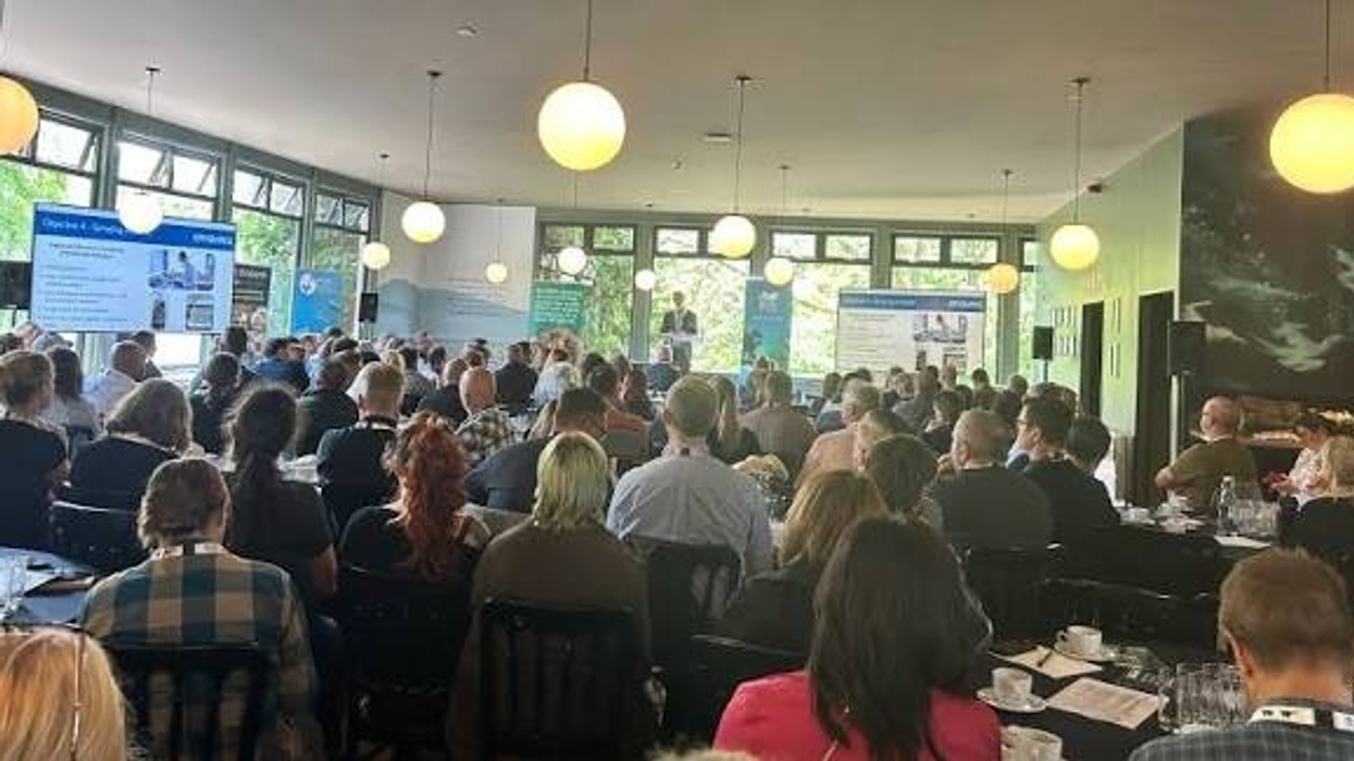 Audience attending a conference in a well-lit room with presentations and speakers.