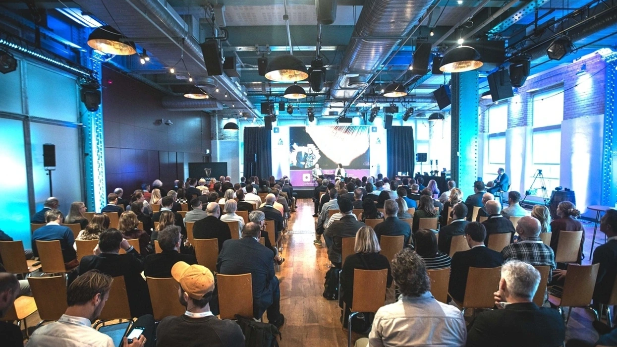 Audience attends a conference in a modern, industrial-style hall with blue lighting.