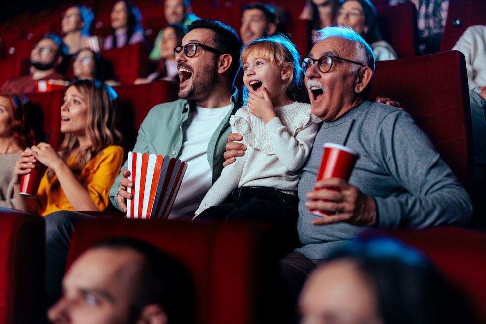 Audience enjoying a movie; diverse group smiling with popcorn and drinks.
