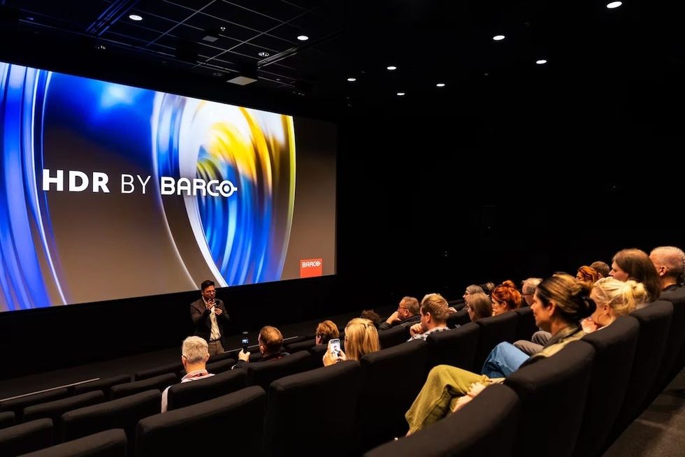 Audience in a cinema watching an "HDR by Barco" presentation on a large screen.