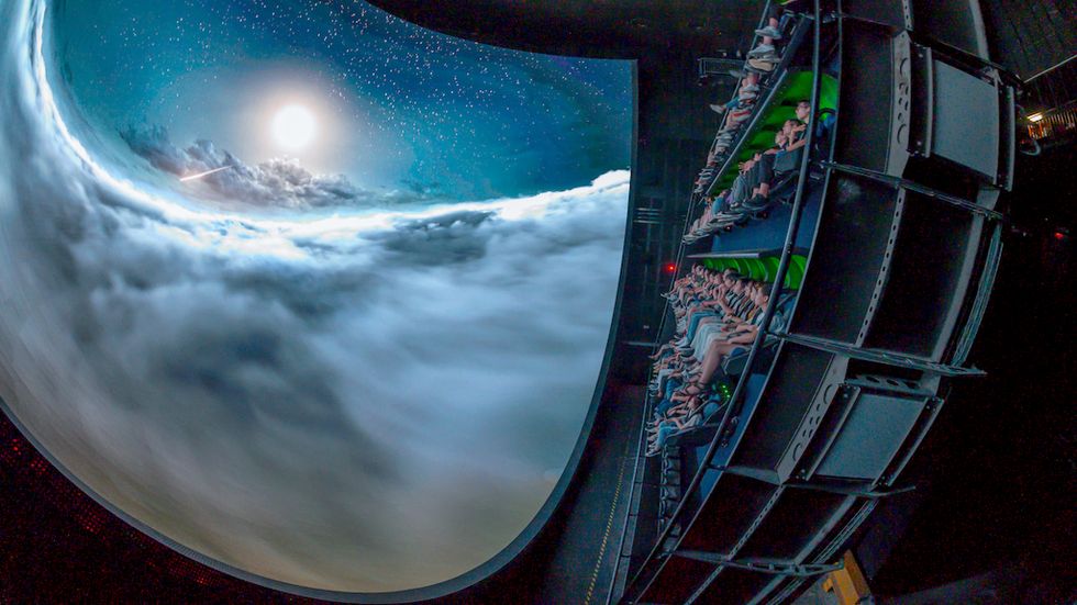 Audience in a curved theater watching clouds and stars on a massive screen.
