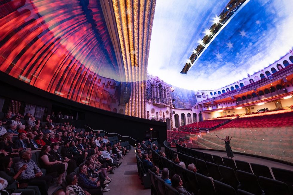 Audience in a planetarium-like theater with a colorful, immersive ceiling projection display.
