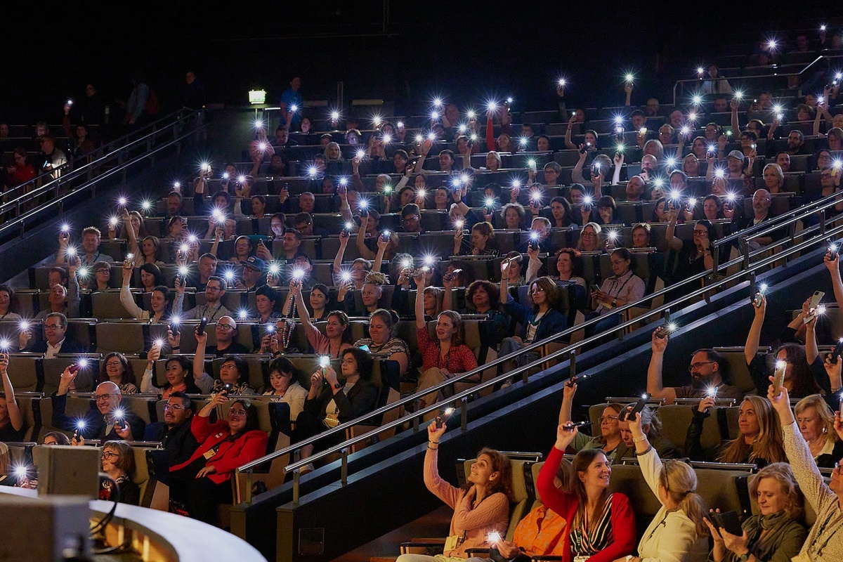 Audience in a theater holding up phones with flashlights on during Ecsite 2026 opening