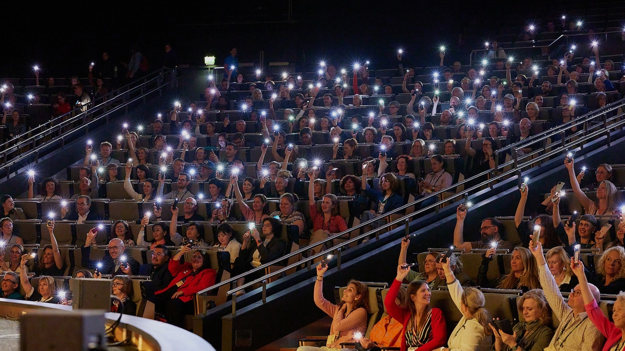 Audience in a theater holding up phones with flashlights on during Ecsite 2026 opening